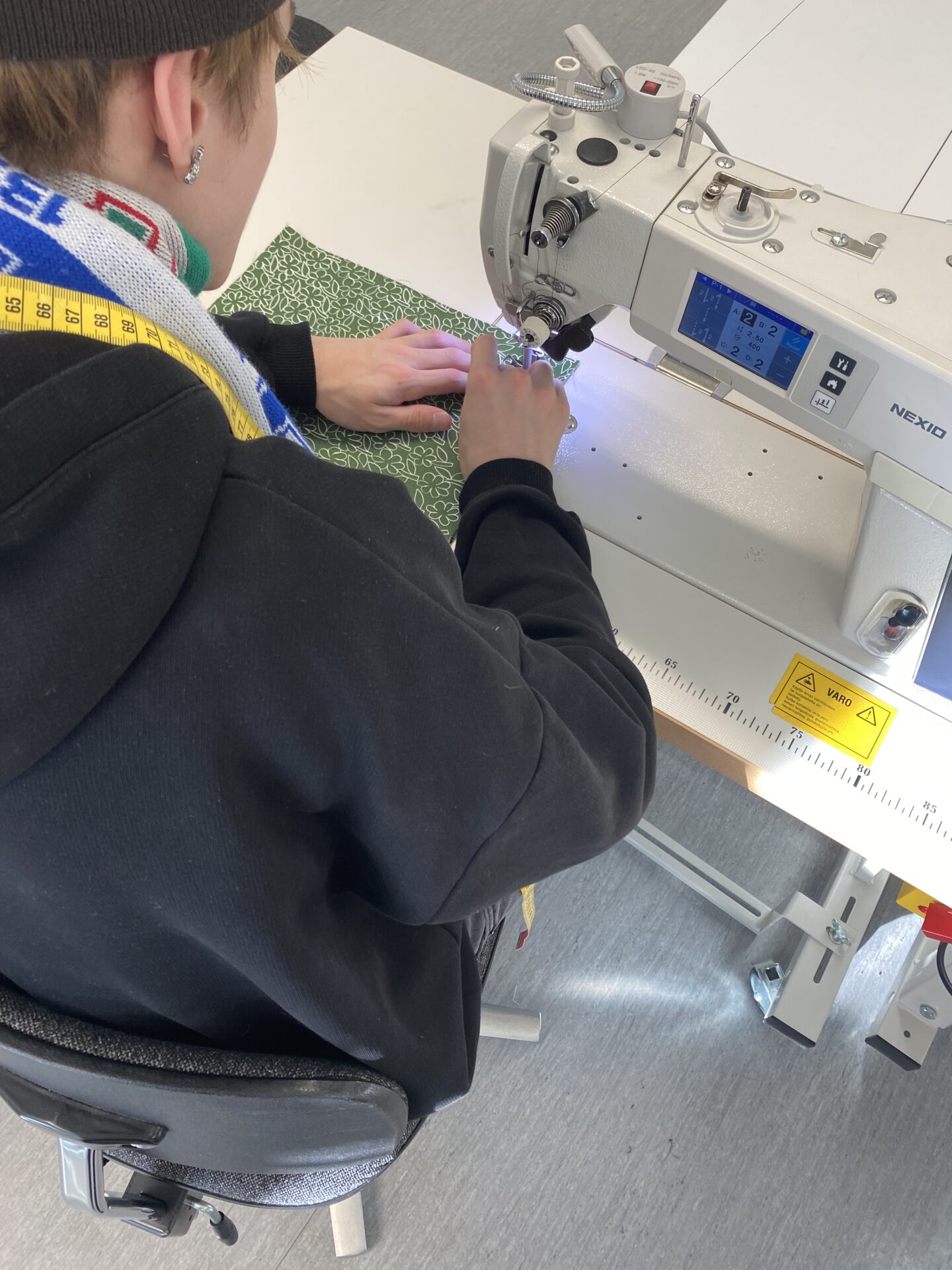 Nuori mies ompelee koneella vihreää Rauha-kuosista kangasta