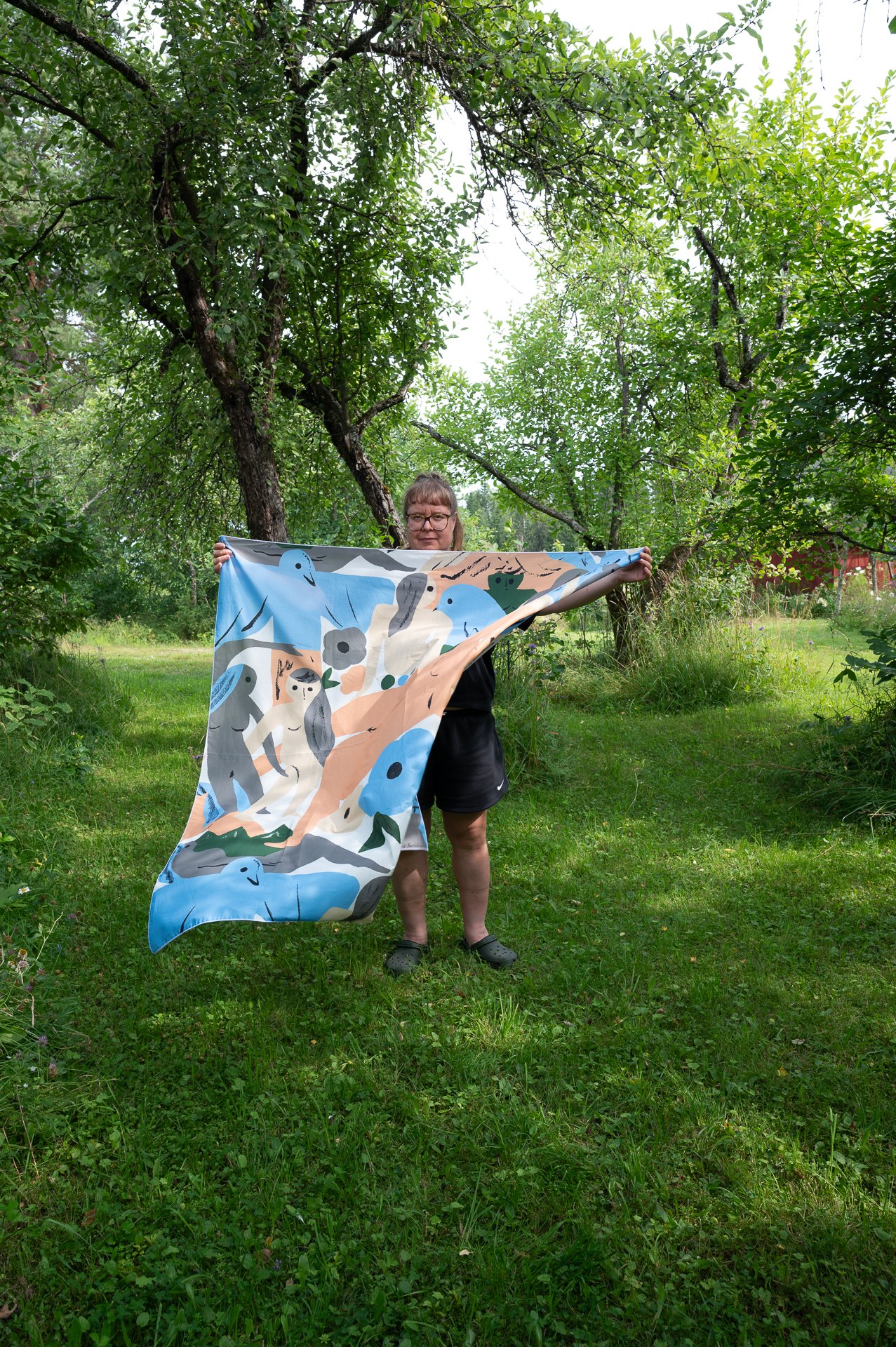 Suunnittelija Jenni Tuominen puutarhassaan pitelee Saunojat-huivia esillä